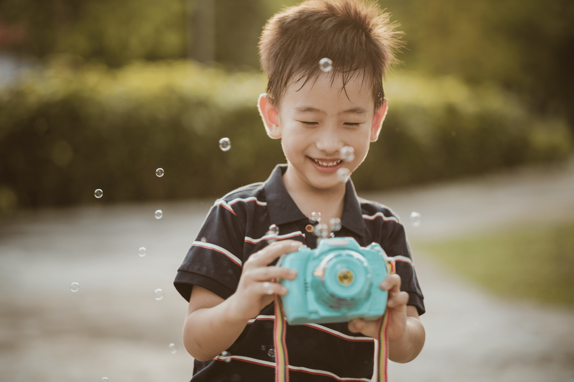a boy holds a toy camera with bubbles floating in frame