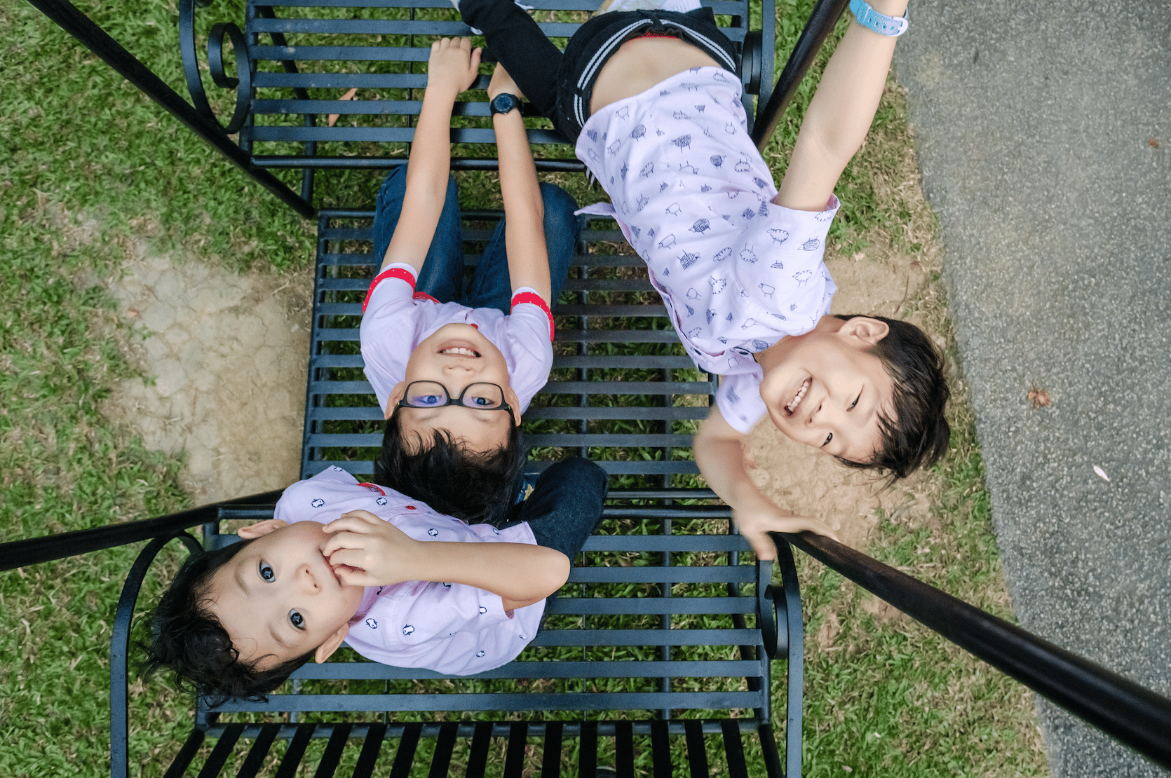 three boys sitting dynamically on a swing smiling upwards at a camera